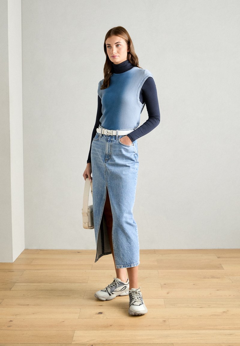 Top sin mangas de canalé azul claro sobre un cuello de tortuga navy, combinado con una falda de mezclilla de tiro alto con una abertura frontal y cinturón blanco.