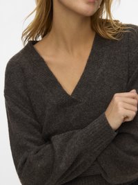 Pull en maille marron foncé avec col en V, manches longues et poignets côtelés. Texture douce et coupe décontractée. Aucun motif ni élément métallique visible.