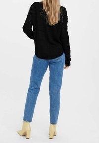 Maglione nero lavorato a maglia, vestibilità rilassata, con maniche lunghe e tessuto testurizzato. Abbinato a jeans blu a gamba dritta e scarpe con tacco a blocco beige.