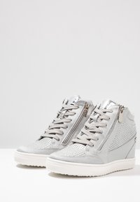 Graue High-Top-Sneaker mit perforiertem Wildleder-Obermaterial, metallischen Akzenten, vorderem Schnürverschluss und seitlichem Reißverschluss, ausgestattet mit einer weißen Gummisohle.