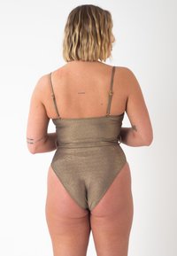 Maillot de bain une pièce doré brillant avec des bretelles fines, une taille cintrée, des jambes échancrées et une texture métallique lisse.