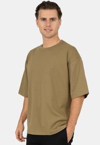 Olijfgroen katoenen T-shirt met een losse pasvorm, korte mouwen en een ronde hals. Soepele textuur met minimale stikseldetails.