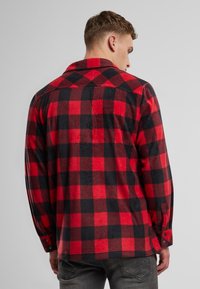 Rotes und schwarzes Karol-Flanellhemd mit entspanntem Kragen, Knopfmanschetten und weicher Textur, von hinten gesehen. Mit einem Rückenpasse-Detail.