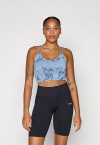Top desportivo azul tie-dye com alças finas e textura suave, combinado com calções altos pretos de tecido canalé. Ambos são roupas atléticas ajustadas ao corpo.