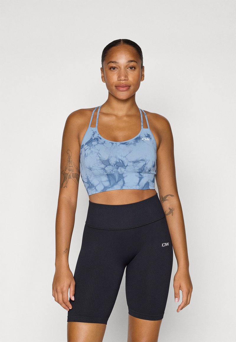 Top desportivo azul tie-dye com alças finas e textura suave, combinado com calções altos pretos de tecido canalé. Ambos são roupas atléticas ajustadas ao corpo.