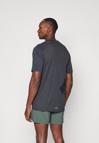 Dark gray athletic shirt with short sleeves and a mesh texture. Visible logo at the bottom. Worn with green shorts.