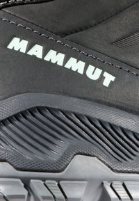 Svart vandringsskor med texturerad gummisula, med varumärket "MAMMUT" i ljus färg. Förstärkt ovandel och detaljerat mönster på sulan.