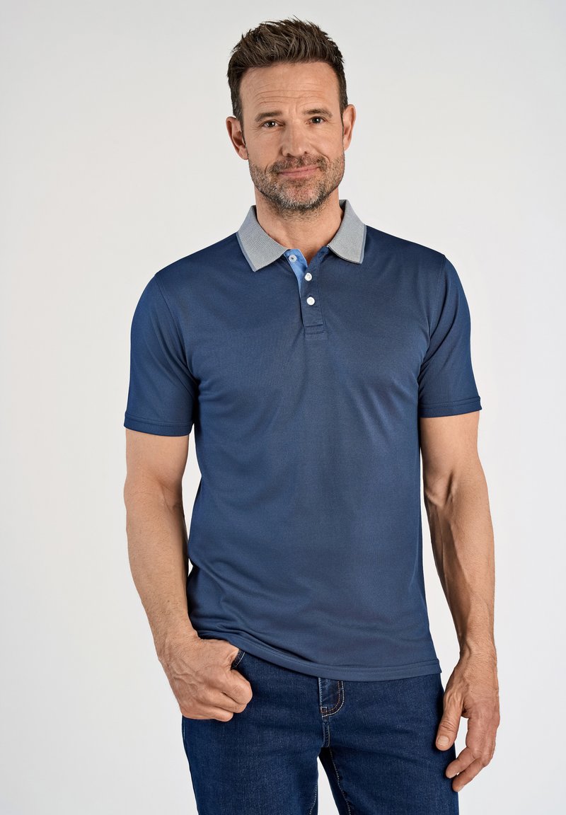 Marineblauwe polo in een zachte stof met een grijze kraag en lichtblauwe knoopaccenten. Beschikt over korte mouwen en een getailleerd ontwerp.