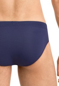 Marineblaue Bade-Unterhosen mit glatter Textur, tief geschnittenem Design und dezenten Nähten. Sitzt eng am Körper und betont die Konturen.