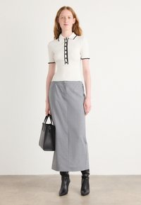 Witte geribbelde polo met zwarte knopen en afwerking, gecombineerd met een grijze kokerrok. Een zwarte handtas en zwarte laarzen tot de knie maken de look compleet.