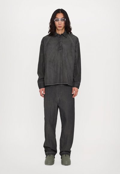 Pull gris foncé texturé avec un col à boutons et des manches longues, associé à un pantalon ample assorti et des chaussures vertes.