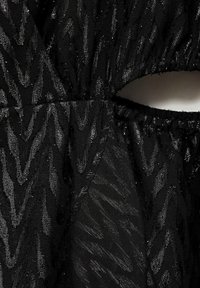 Czarna sukienka z teksturowanej tkaniny w wzór zygzakowy, subtelny połysk oraz wycięcie w talii. Zgromadzony elastyczny pas.