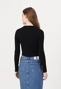 Schwarzes, geripptes Langarmoberteil mit rundem Halsausschnitt, kombiniert mit einem Jeansrock, der ein Logoetikett am Bund und Gesäßtaschen aufweist.