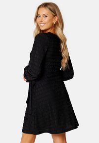 Schwarzes, strukturiertes Kleid mit langen Ärmeln und schmalem Taillengürtel. Ausgestellter Rock und subtile Raffungselemente überall. Elegantes und vielseitiges Design.