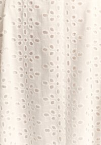 Balta audinys su tekstūruotu raštu, kuriame tolygiai išdėstyti ovalios formos išpjovos, apjuostos siuvinėtų dygsnių kontūrais, sukuriantys švelnų įspūdį.