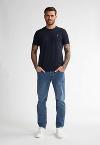 Granatowy bawełniany T-shirt z krótkimi rękawami, okrągłym dekoltem i małym logo. W zestawie z jasnoniebieskimi jeansami i białymi trampkami.