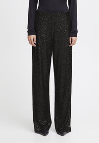 Pantalon larges noirs à sequins avec une texture lisse et une taille haute, comportant des ornements verticaux et une silhouette fluide.