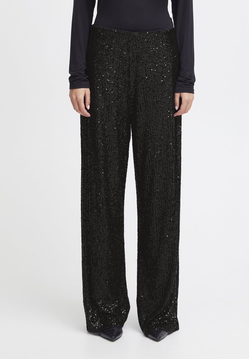Pantalon larges noirs à sequins avec une texture lisse et une taille haute, comportant des ornements verticaux et une silhouette fluide.
