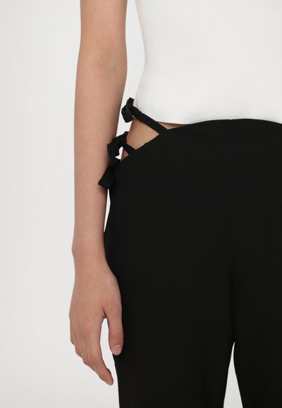 Zwarte op maat gemaakte broek met een uitsnede aan de zijkant en stoffen strikken op de taille. Gecombineerd met een aansluitend wit shirt met een gestructureerde afwerking.