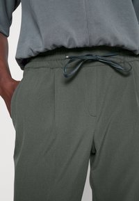 Mörkgröna, lätta byxor med elastisk midja, snördetalj och sidofickor, med en slät och stilren tygstruktur.