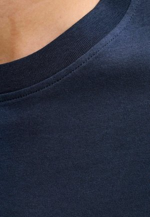 Close-up van de nek en schouder van een persoon die een donkerblauw katoenen T-shirt met ronde hals en zichtbare naden draagt.