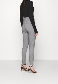Černý dlouhý rukáv top spárovaný s černobíle kostkovanými kalhotami s vysokým pasem a černými stiletto sandály, které vystihují elegantní siluetu.