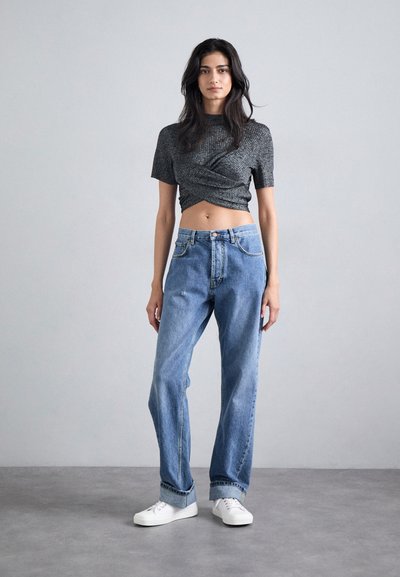Svart kortärmad omslagstopp med texturerad design som kombineras med ljusblå högmidjade jeans. Vita sneakers fulländar looken.