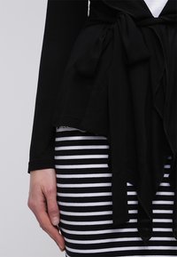 Černý top s detailním uvázáním v pase, ve spojení s černobílou pruhovanou sukní. Top má dlouhé rukávy a volný střih.