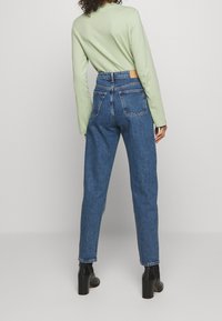 Siniset korkeavyötäröiset farkut rentoa istuvuutta, joissa on neljä taskua ja kontrastivärinen ommel, yhdistettynä vaaleanvihreään pitkähiharaiseen paitaan.