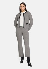 Costume noir et blanc texturé avec un motif à carreaux ; veste cintrée avec boutons à l'avant, associée à un pantalon droit et des bottines noires.