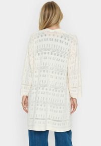 Ljuscremefärgad lång cardigan med öppen stickad struktur, 3/4 ärmar och en avslappnad passform, med blommönster och geometriska mönster genom hela.