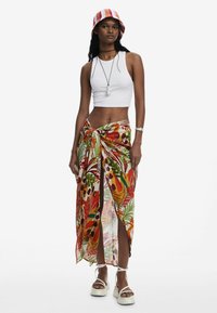 Crop top in tessuto bianco, abbinato a una lunga gonna colorata con stampa floreale annodata in vita, dotata di spacchi. Sandali platform bianchi.