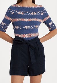 Top corto de estampado azul con rayas claras y oscuras, combinado con pantalones cortos oscuros que tienen un cinturón atado y bolsillos laterales.