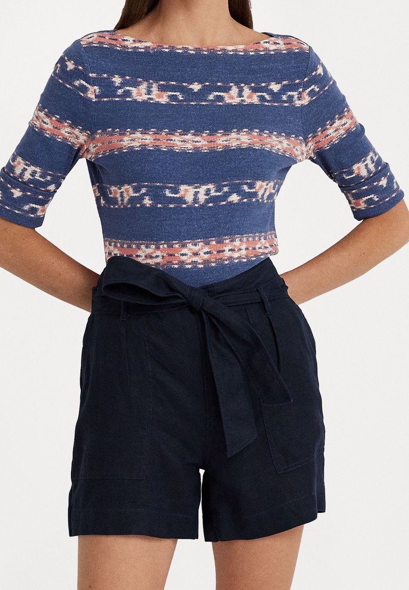 Top corto de estampado azul con rayas claras y oscuras, combinado con pantalones cortos oscuros que tienen un cinturón atado y bolsillos laterales.