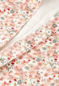 Tela con estampado floral en suaves tonos pastel de rosa, rojo y verde. Presenta cierres a presión plateados en el frente y una textura suave.