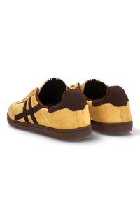 Zapatillas de ante en amarillo con detalles en marrón. Presentan una superficie texturizada, rayas en contraste y una suela de goma con un talón redondeado.