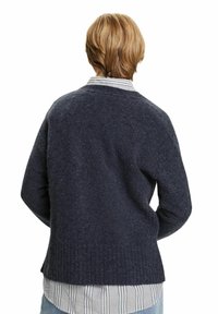 Navy gestrickter Pullover mit strukturiertem Muster, rundem Ausschnitt, geripptem Saum und lockerer Passform, getragen über einem weiß-blau gestreiften Hemd.
