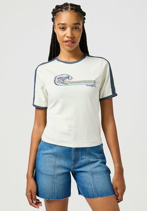 Camiseta crema de manga corta con ribete en oscuro azul en contraste y un gráfico de ola de surf, combinada con pantalones cortos de mezclilla con dobladillo deshilachado.