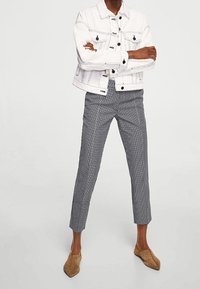 Veste en denim blanche avec des coutures noires, associée à un pantalon cropped à carreaux gris et blancs, et des mules en suède beige.