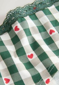 Green and white checked fabric with red heart patterns, featuring a delicate green lace trim along the top edge. Soft, textured material.