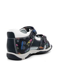 Sandali neri con motivi colorati di monster truck, doppi strap in Velcro, tallone e dettagli bianchi e una suola in gomma texturizzata per una migliore aderenza.