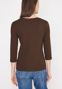 Top marrone a tre quarti di manica realizzato in tessuto morbido, con scollo rotondo e superficie liscia, abbinato a jeans in denim blu.