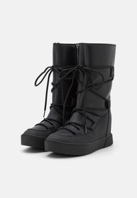 Svarta ankelskor i texturerat syntetmaterial har snörning framtill och en sidodragkedja för stängning. Tjock gummisul med ribbad detalj.