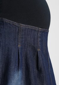 Falda de mezclilla con un diseño plisado, que cuenta con una cinturilla elástica negra, tela de mezclilla azul, costuras visibles y una silueta ligeramente acampanada.