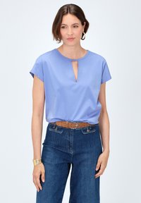 Lichtblauw kort mouwtop met een keyhole halslijn, gecombineerd met donkerblauwe hoge taille jeans en een broekriem van bruin leer. Gelaagde armband gedragen.