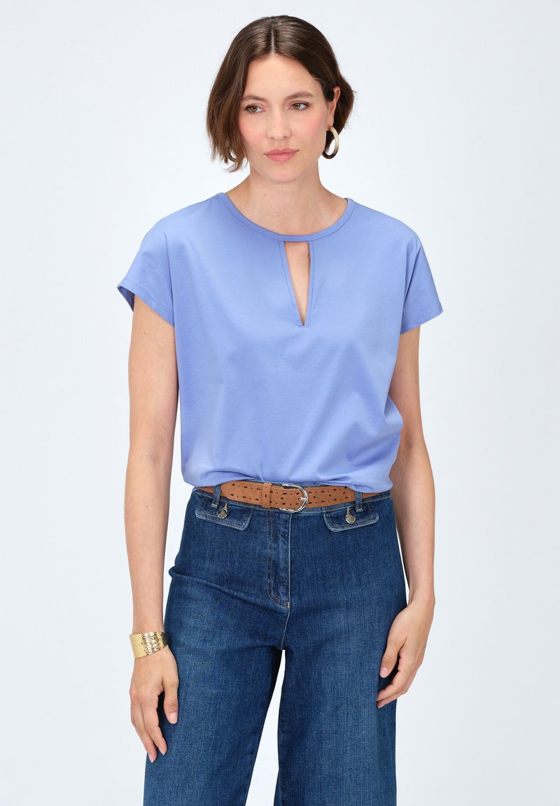 Lichtblauw kort mouwtop met een keyhole halslijn, gecombineerd met donkerblauwe hoge taille jeans en een broekriem van bruin leer. Gelaagde armband gedragen.