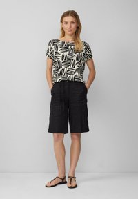 Korte mouwen top in crème met een zwart bladerenpatroon, gecombineerd met zwarte linnen short met een trekkoord in de taille en twee zijzakken.