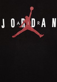 Svart t-shirt med en stor röd siluett av en basketspelare som hoppar, med ordet "JORDAN" i tjocka vita bokstäver.