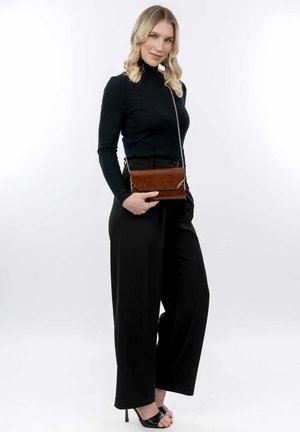 Bruine leren crossbody tas met een kettingband, voorzien van een slanke rechthoekige vorm en subtiele stikseldetails, gecombineerd met zwarte wijde pantalon.