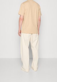 Camiseta de algodón beige de manga corta, combinada con pantalones holgados de color blanco roto. Diseño simple, con mínimos detalles de costura.